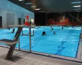 Menschen schwimmen im **Gartenhallenbad Enger**. Ein Sprungbrett mit einem orange-weißen Kegel steht am Beckenrand.