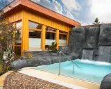 Entspannendes Wasserbecken mit Wasserfällen vor einer Holzhütte, ideal für eine H2O Sauna.