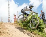 Downhill-Fahrer springt über eine Schanze bei den Dirt Masters Winterberg. Zuschauer beobachten das Spektakel.