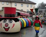 Bunter Karnevalsumzug mit einem riesigen Clown-Motivwagen und kostümierten Menschen. Die Karnevalstage sind voller Freude und bunter Kostüme.