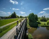 Zwei Radfahrer genießen die Aussicht auf der hohen Mark Radroute über eine Brücke, umgeben von grünen Wiesen und Bäumen.