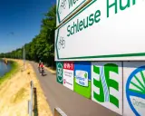 Radwegweiser am Schleusenweg zeigen den Verlauf des Emsland-Radwegs. Radfahrer genießen die Fahrt entlang des Kanals.