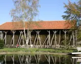 Große Gradierwerke mit roten Ziegeldächern, umgeben von Bäumen und einem Teich. Hier wird die Luft mit gesundem **saline rheine** angereichert.