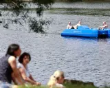Sommerliche Ausblicke rund um Heiligenhaus: Menschen genießen den Tag am See, während drei Männer in einem blauen Tretboot über das Wasser gleiten.