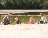 Familie spielt am Sandstrand des badesee mindenerwald. Vater hilft Sohn beim Sandburgen bauen, während Mutter und Tochter daneben sitzen.