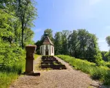 Ein kleiner Weg führt zu einer Kapelle auf einem Hügel, umgeben von grünen Bäumen. Der schmetterlingspfad willebadessen lädt zum Entdecken ein.