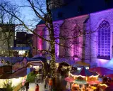 Bunte Lichter und Buden auf dem weihnachtsmarkt werne. Eine Kirche im Hintergrund erstrahlt in lila Licht.
