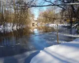 Winterliche Idylle an der **Planwiese Telgte**: Eisiger Fluss, schneebedeckte Ufer und ein Fachwerkhaus spiegeln sich im Wasser.