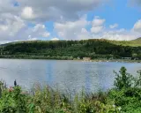 Idyllische Landschaft am Emmer-Radweg mit See, bewaldeten Hügeln und einigen Anglern am Ufer.
