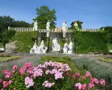 Prachtvoller Brunnen mit Skulpturen und Wasserfällen, umgeben von blühenden Blumen und Grün im botanischen Garten NRW.