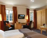 Gemütliches Zimmer mit Blick auf die Klosterpforte Harsewinkel. Einladende Sessel, Schreibtisch und ein großes Bett.