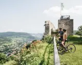 Zwei Radreisende genießen den Ausblick auf ein Tal mit einer Stadt und Ruinen. Perfekt für eine 5-tägige Radreise Deutschland.