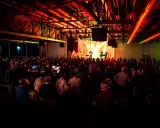 Ein Konzert in Emsdetten mit einer Band auf der Bühne und vielen begeisterten Zuschauern. Die Beleuchtung taucht die Szene in ein warmes, rotes Licht.