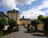 Schloss Wittgenstein in Bad Laasphe, ein gelbes Barockschloss mit Turm, umgeben von Bäumen und einem blauen Himmel mit Wolken.