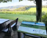 Holzbänke und ein Tisch laden zum Verweilen ein. Ein Schild "Familienplatz - Weg der Blicke" weist auf die Aussicht hin.