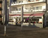 Geschlossene Sonnenschirme säumen die rheinpromenade emmerich. Ein Restaurant mit "OPEN"-Schild lädt zum Verweilen ein.