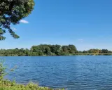 Blauer Himmel über dem ruhigen Linteler See, umgeben von üppigem Grün.