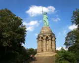 Aufstieg zum Hermannsdenkmal: Wanderer erklimmen die Stufen zum imposanten Reiterstandbild unter blauem Himmel.