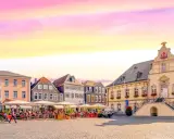 Ein Marktplatz mit Cafés und historischen Gebäuden, der an das "Venedig Westfalens" erinnert, unter einem farbenfrohen Himmel.