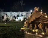 Bethlehemskrippe mit Figuren und Lichtern auf dem weihnachtsmarkt legden. Im Hintergrund eine Person mit Rollator und Lichterketten.