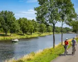 Zwei Radfahrer genießen eine Tour auf dem Dortmund-Ems-Kanal-Radweg. Ein kleines Boot fährt auf dem Wasser.