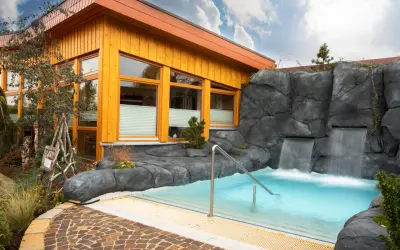 Entspannendes Wasserbecken mit Wasserfällen vor einer Holzhütte, ideal für eine H2O Sauna.