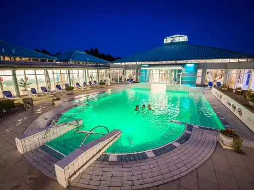 Abendliche Erfrischung im beleuchteten Pool der Therme Bad Driburg. Drei Personen genießen das warme Wasser unter dem klaren Nachthimmel.