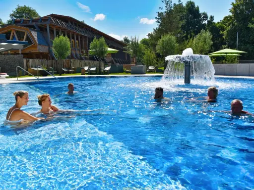 Entspannte Menschen genießen das Schwimmbad eines Kurortes in NRW. Ein Wasserspiel sorgt für Erfrischung.