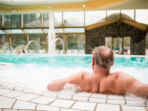Entspannter Mann genießt das sprudelnde Wasser im mattlerbusch schwimmbad. Hinter ihm ein großes Becken mit Wasserspielen und viel Glas.