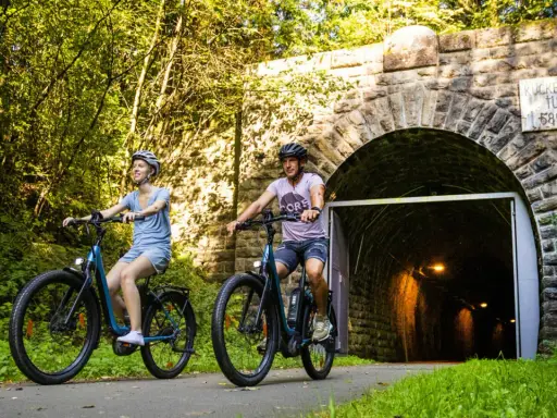 Ein Paar genießt eine entspannte Sauerland Fahrradtour, radelt auf E-Bikes am Eingang des Kuckelheimer Tunnels entlang.