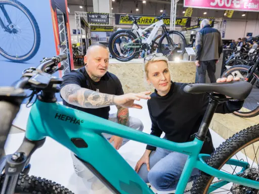 Ein Mann mit Tattoos und eine Frau begutachten auf der Fahrrad Messe ein türkisfarbenes E-Bike.