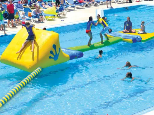 Kinder spielen auf einer aufblasbaren Wasserrutsche und im Pool eines Freibades.