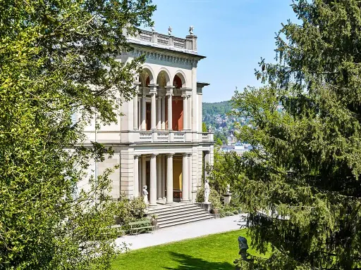 Prachtvolles Gebäude mit Säulen und Arkaden, umgeben von grünen Bäumen. Ein schöner Ort, um Kunst zu genießen, wie im Museum Rietberg.