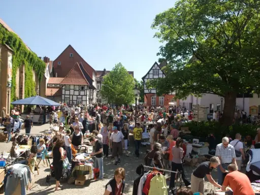 Buntes Treiben auf dem Flohmarkt Minden. Menschen stöbern an Ständen mit Kleidung und Trödel vor Fachwerkhäusern.