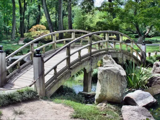Eine hölzerne Bogenbrücke führt durch den grünen Herford Park. Ein kleiner Bach plätschert unter der Brücke hindurch.