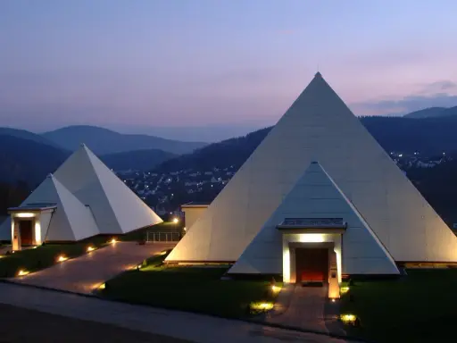 Zwei moderne Pyramiden im Sauerland, beleuchtet im Abendlicht, mit einem Dorf im Hintergrund.