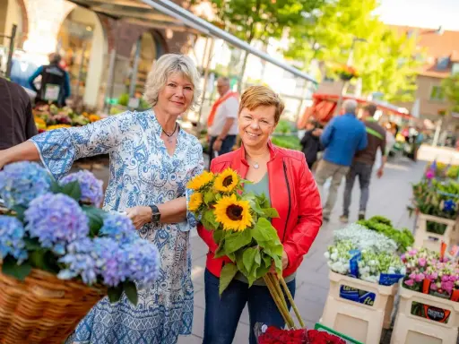 Zwei Frauen mit Blumen auf dem Markt in Coesfeld. Eine hält Sonnenblumen, die andere hat Hortensien im Fahrradkorb.