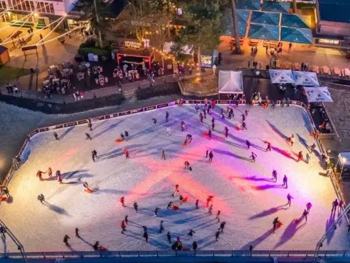 Ein belebter weihnachtsmarkt mit schlittschuhbahn. Menschen gleiten über das Eis, während Lichter die Szene in warme Farben tauchen.