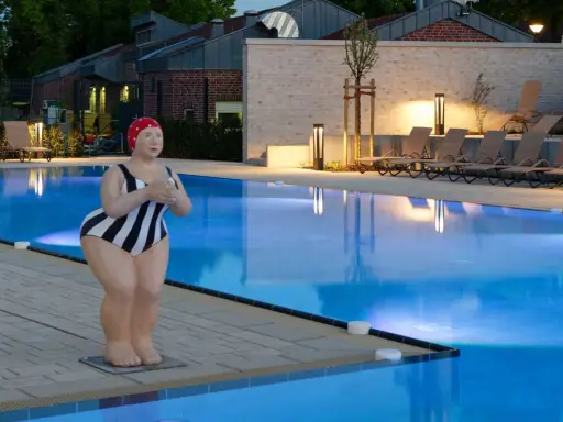 Skulptur einer Schwimmerin am beleuchteten Pool des Solebads Werne. Liegestühle und Bäume säumen das Becken.