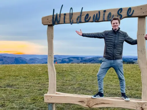 Ein Mann steht vor einem Holzrahmen mit der Aufschrift "Wildewiese". Ein toller Ort für fotospots nrw bei Sonnenuntergang.