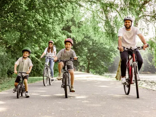 Familie genießt eine Fahrradtour mit Kindern in NRW. Vater, Mutter und zwei Jungen radeln auf einem asphaltierten Weg durch eine grüne Allee.