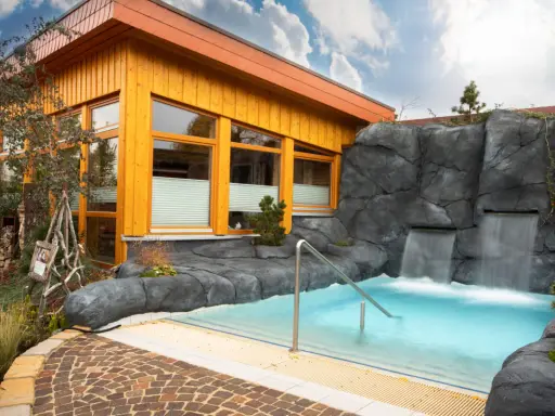 Entspannendes Wasserbecken mit Wasserfällen vor einer Holzhütte, ideal für eine H2O Sauna.