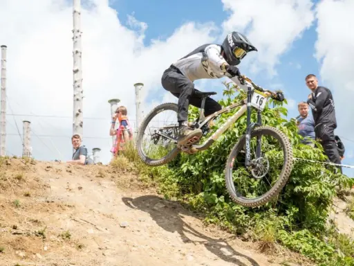 Downhill-Fahrer springt über eine Schanze bei den Dirt Masters Winterberg. Zuschauer beobachten das Spektakel.