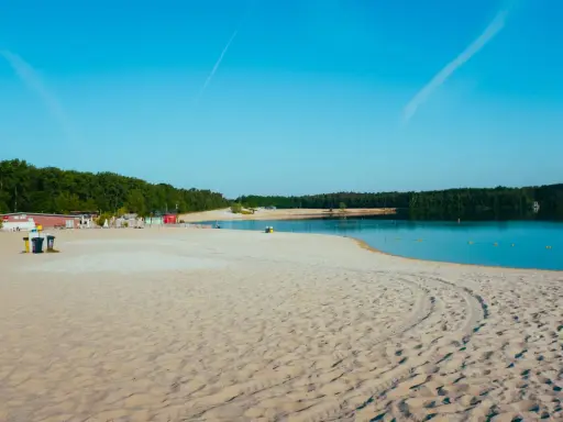 Sonniger Strand in NRW mit feinem Sand, klarem Wasser und grünen Bäumen im Hintergrund. Perfekt für einen entspannten Tag am See.