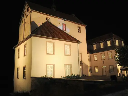 Die beleuchtete Dreckburg in Salzkotten bei Nacht. Ein imposantes Gebäude mit vielen Fenstern und einem dunklen Himmel.