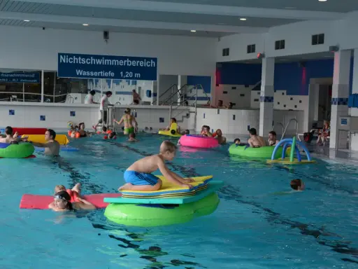 Kinder und Erwachsene planschen im Nichtschwimmerbereich des Schwimmbads Brakel. Viele nutzen bunte Schwimmtiere und Matten.