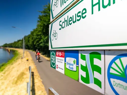 Radwegweiser am Schleusenweg zeigen den Verlauf des Emsland-Radwegs. Radfahrer genießen die Fahrt entlang des Kanals.