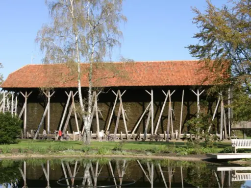 Große Gradierwerke mit roten Ziegeldächern, umgeben von Bäumen und einem Teich. Hier wird die Luft mit gesundem **saline rheine** angereichert.