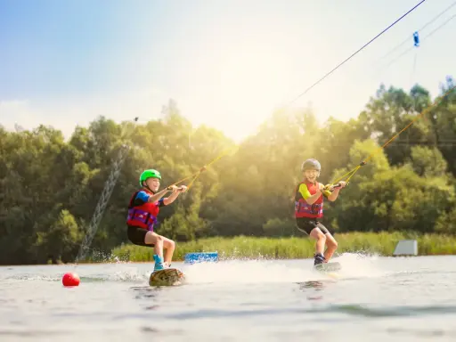 Zwei Kinder üben Wakeboarden am Nesthauser See, gezogen von einer Seilbahn.