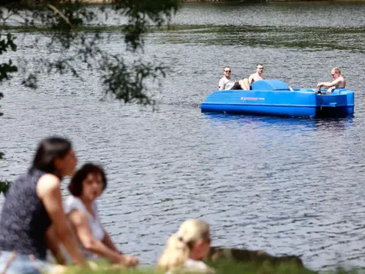 Sommerliche Ausblicke rund um Heiligenhaus: Menschen genießen den Tag am See, während drei Männer in einem blauen Tretboot über das Wasser gleiten.